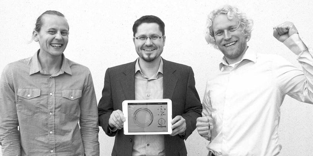 Three men standing together holding a tablet computer.