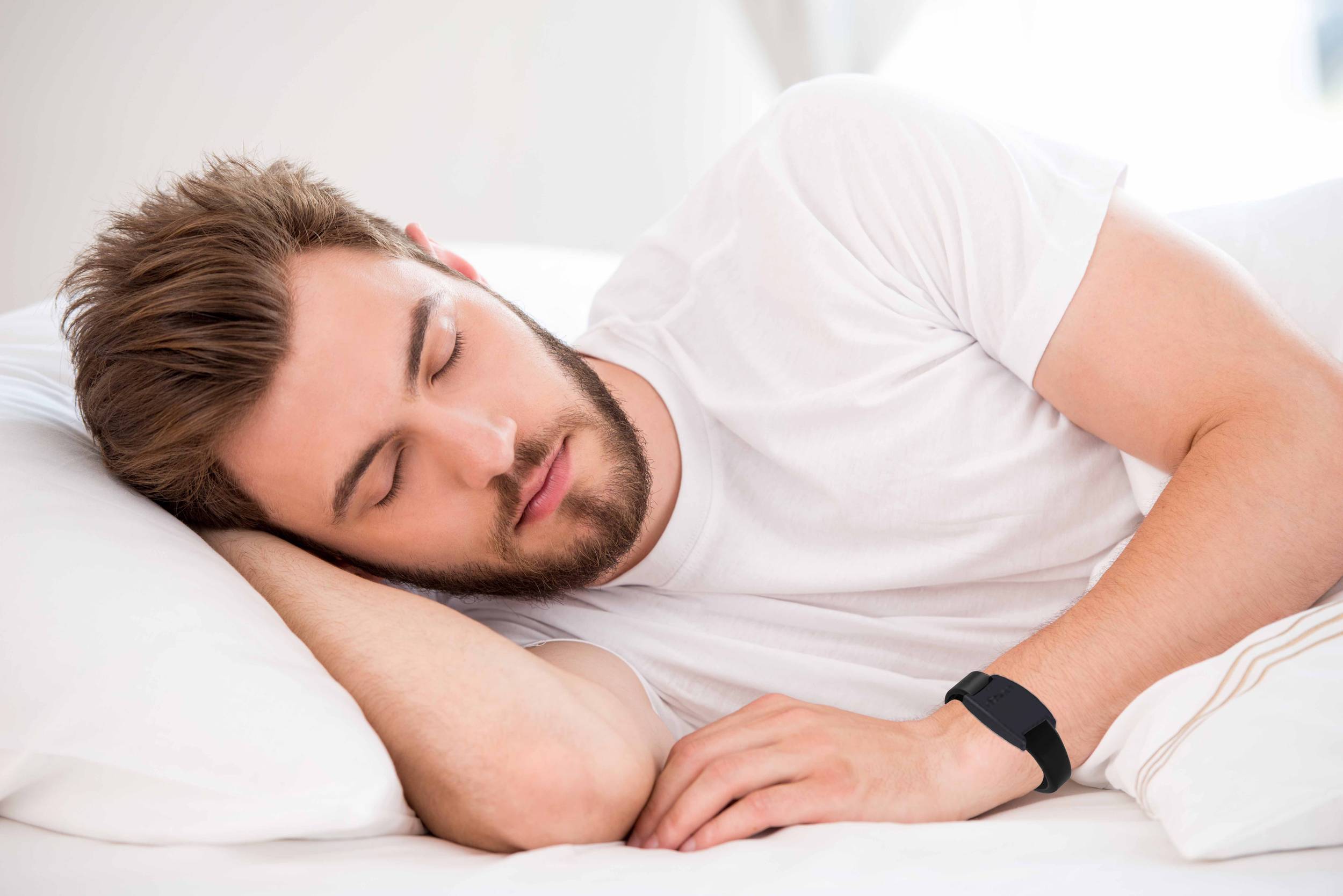 A man in deep sleep on a white bed with a watch on his wrist.