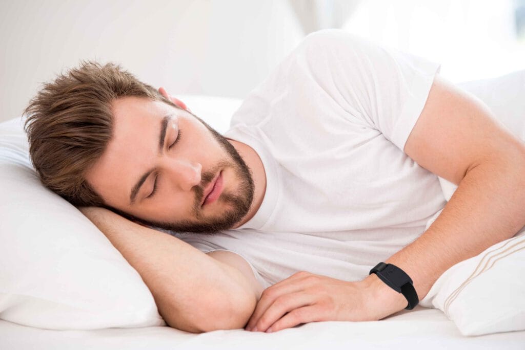 A man sleeping on a white bed with a watch on his wrist.