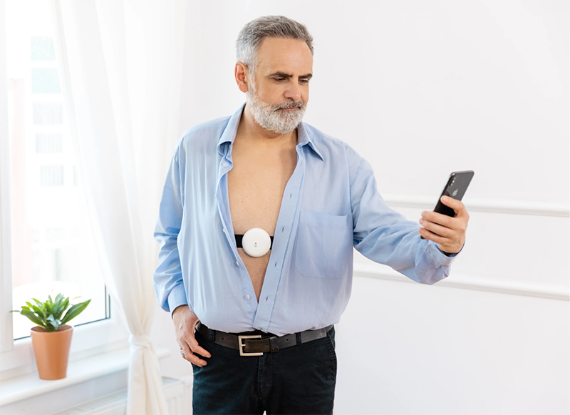 Man watching smart phone and wearing Fibion Vitals wearable on chest
