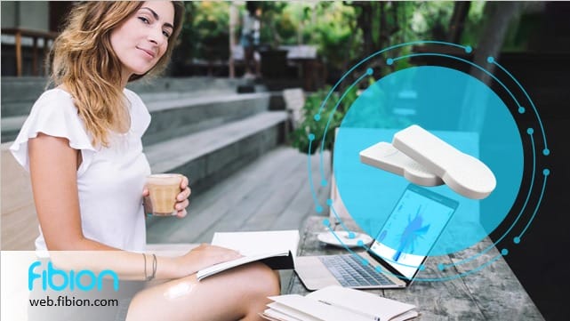 Woman sitting outdoors with a laptop and notebook, holding a drink. An overlay graphic shows wearable devices, highlighting the Fibion SENS for an all-in-one Motion Test. Fibion logo and website URL are at the bottom of the image.