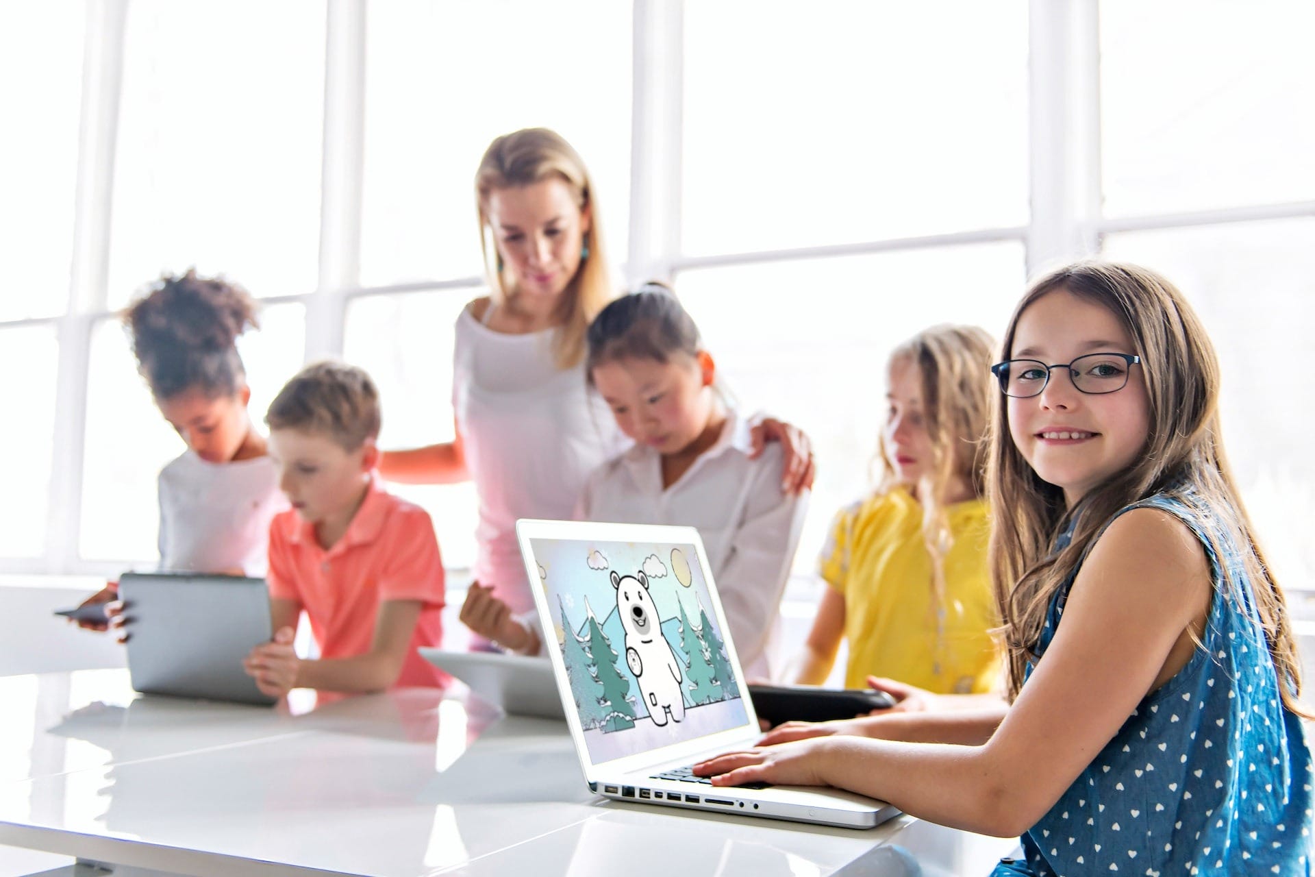 A group of children engaged in a science project using laptops at a table with a female adult supervising.