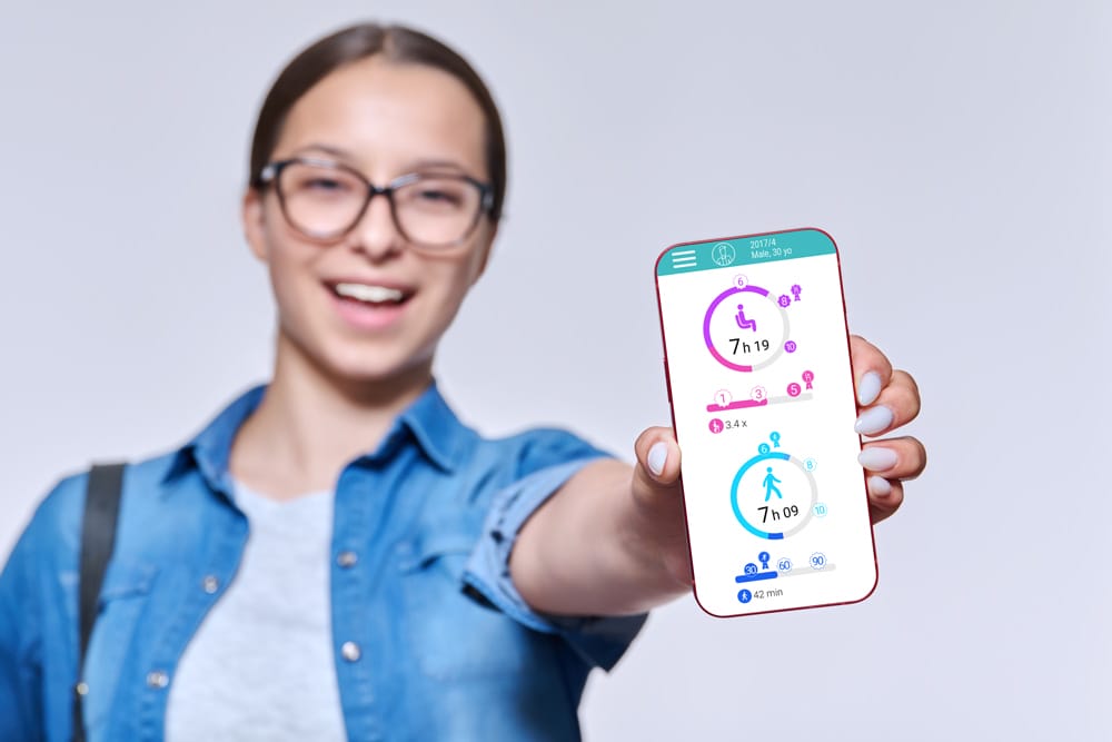 A smiling woman wearing glasses holds out a smartphone displaying the Fibion fitness app, focusing the screen towards the viewer.