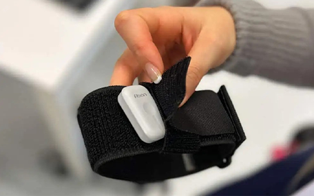 A person holds a black fabric strap with a small white Gen2 Fibion Device attached to it.