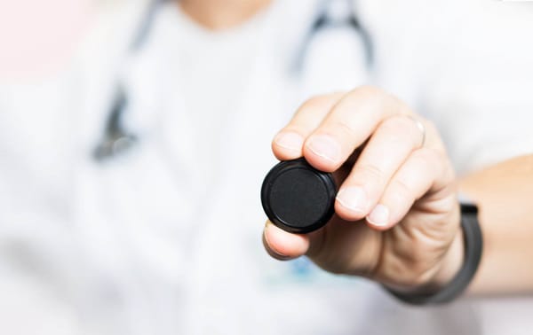 A person wearing a white coat holds a stethoscope diaphragm towards the camera, capturing the moment like a flash.