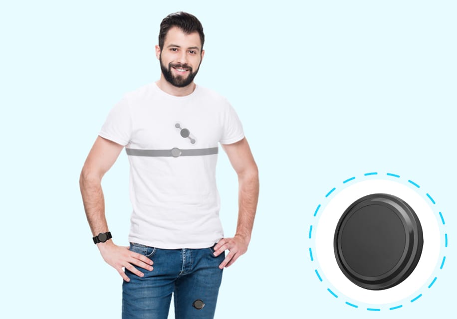 A man is wearing a white t-shirt with a chest strap, standing beside a large round black device, possibly from Fibion Solutions, for research on circadian rhythm.