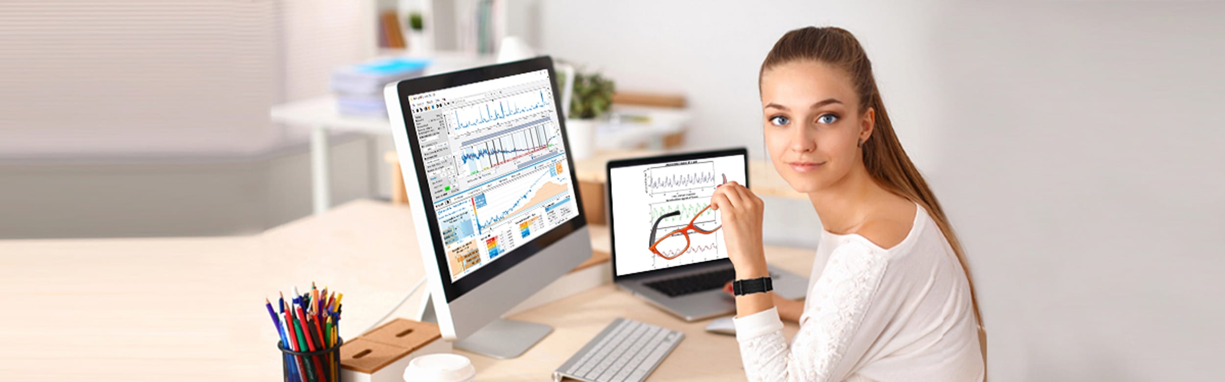 A woman sits at her desk, surrounded by computers displaying graphs and data, contemplating solutions to incorporate more physical activity into her sedentary work routine.