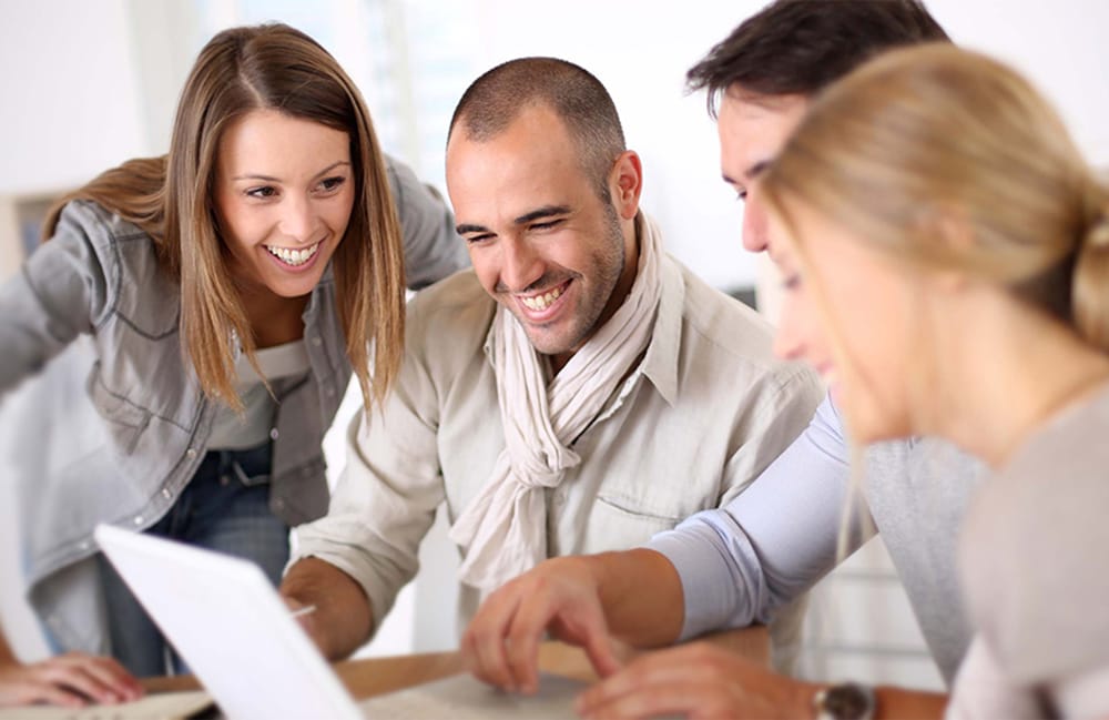 Four people are smiling and working together around a laptop, exploring innovative solutions with the power of SENS Motion.