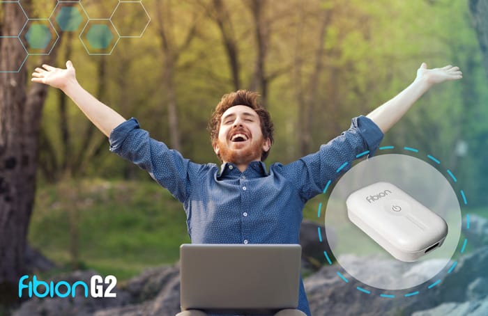 Man sitting outdoors with arms raised, sitting in front of a laptop. Image of Fibion G2 device is shown beside him.